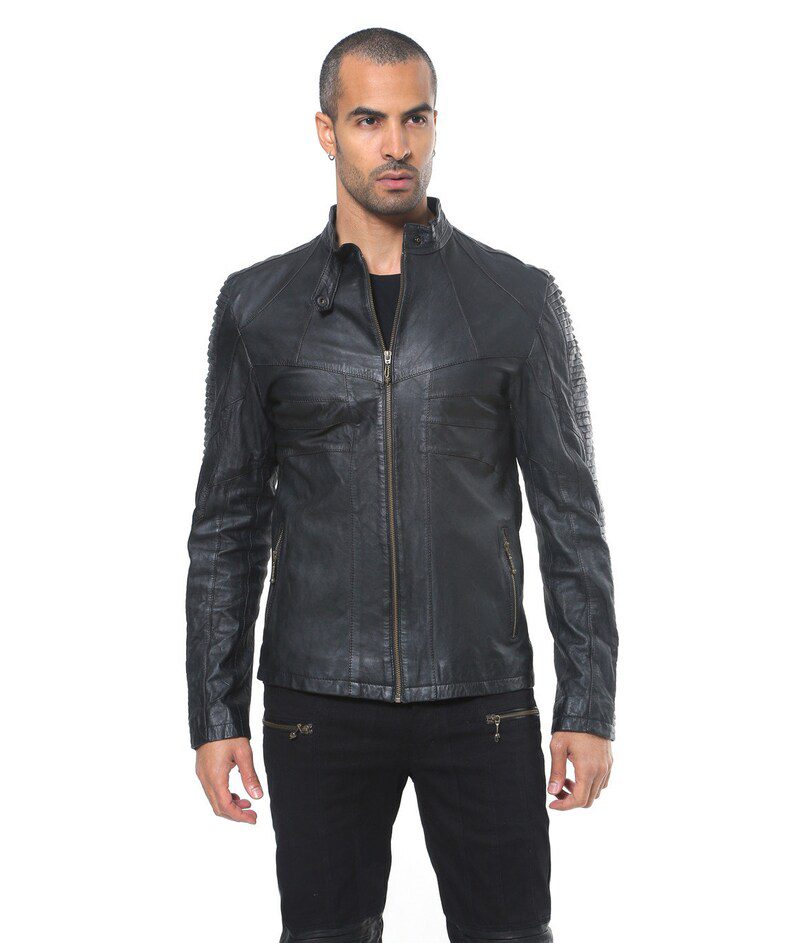 Lambskin Leather Jacket | Ribbed Black Leather Jacket A front-facing photo of a man wearing a black leather jacket with a central silver zipper slightly open, paired with black pants, featuring tactical quilted sleeves and a streamlined collar.