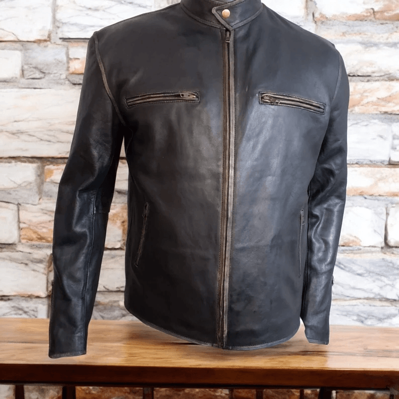 A front view of a dark, vintage-style leather jacket on a mannequin, highlighting the mandarin-style collar with a snap-button closure and two zippered chest pockets.