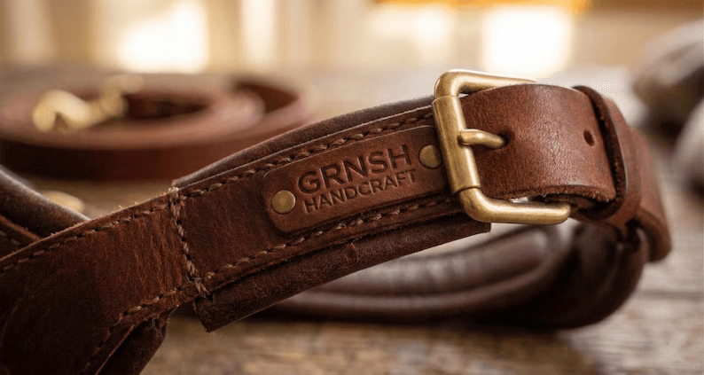 A close-up detail shot of the GRNSH Handcraft leather dog harness showing the embossed brand logo, high-quality stitching, and antique brass buckle