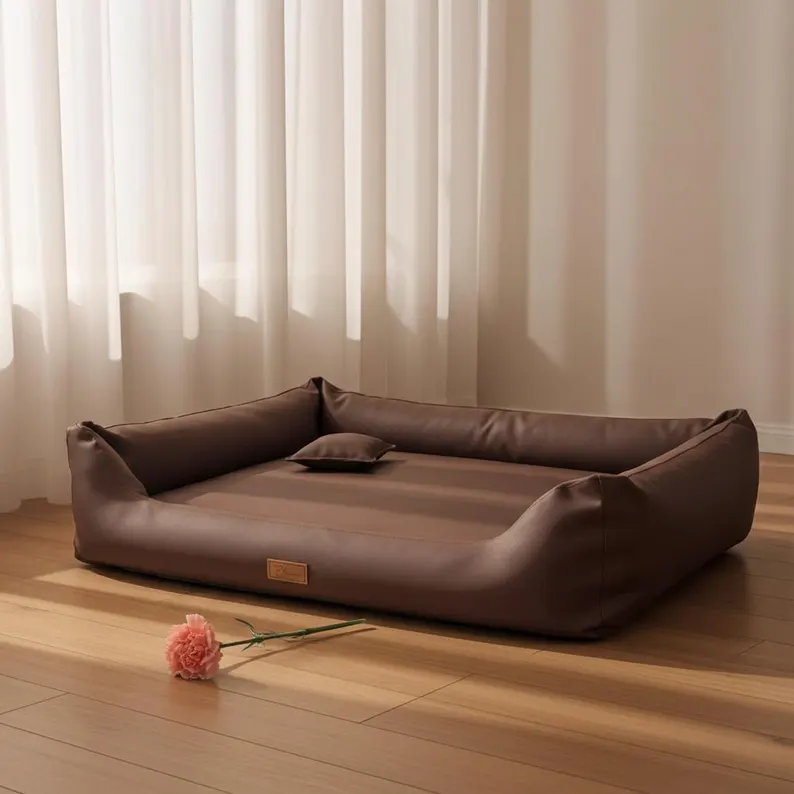 Leather Dog Bed | Luxury Handmade Pet Sofa A minimalist leather dog bed in chocolate brown, featuring raised bolstered edges and a matching small pillow, positioned on a light wood floor near sunlit white curtains.