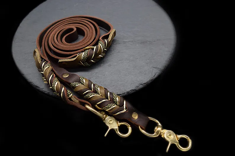 Leather Dog Leash | Full Grain Leather Lead Braided A high-quality brown Leather Dog Leash coiled on a dark grey slate surface. The leash features intricate hand-woven braiding with gold and olive-patterned accents near the heavy-duty brass trigger snaps.