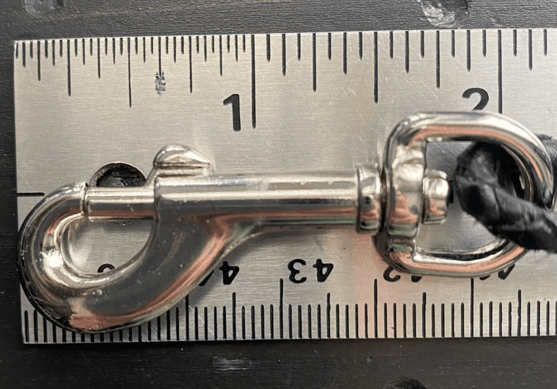 Leather Dog Leash | Braided Kangaroo Leather Dog Show Lead A close-up shot of the silver metal swivel bolt snap clasp laid against a metal ruler. The clasp measures approximately 2 inches in length.