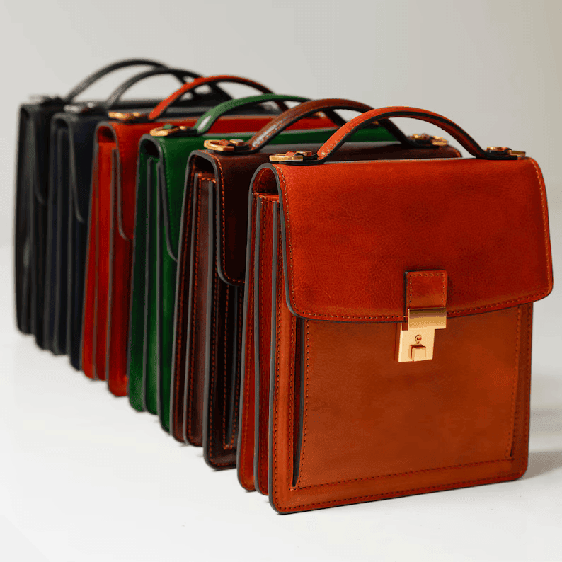 A line-up of small leather briefcases and handbags displayed in various colors including tan brown, dark brown, green, red, navy, and black on a clean white surface.